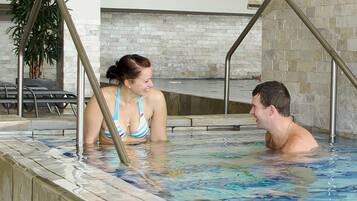 Un hombre y una mujer en una piscina con barandillas de metal y una pared de piedra al fondo.