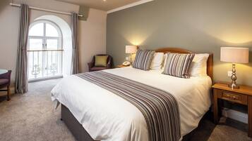 Habitación de hotel con una cama grande, dos lámparas de noche, una silla, un escritorio y una ventana con cortinas.