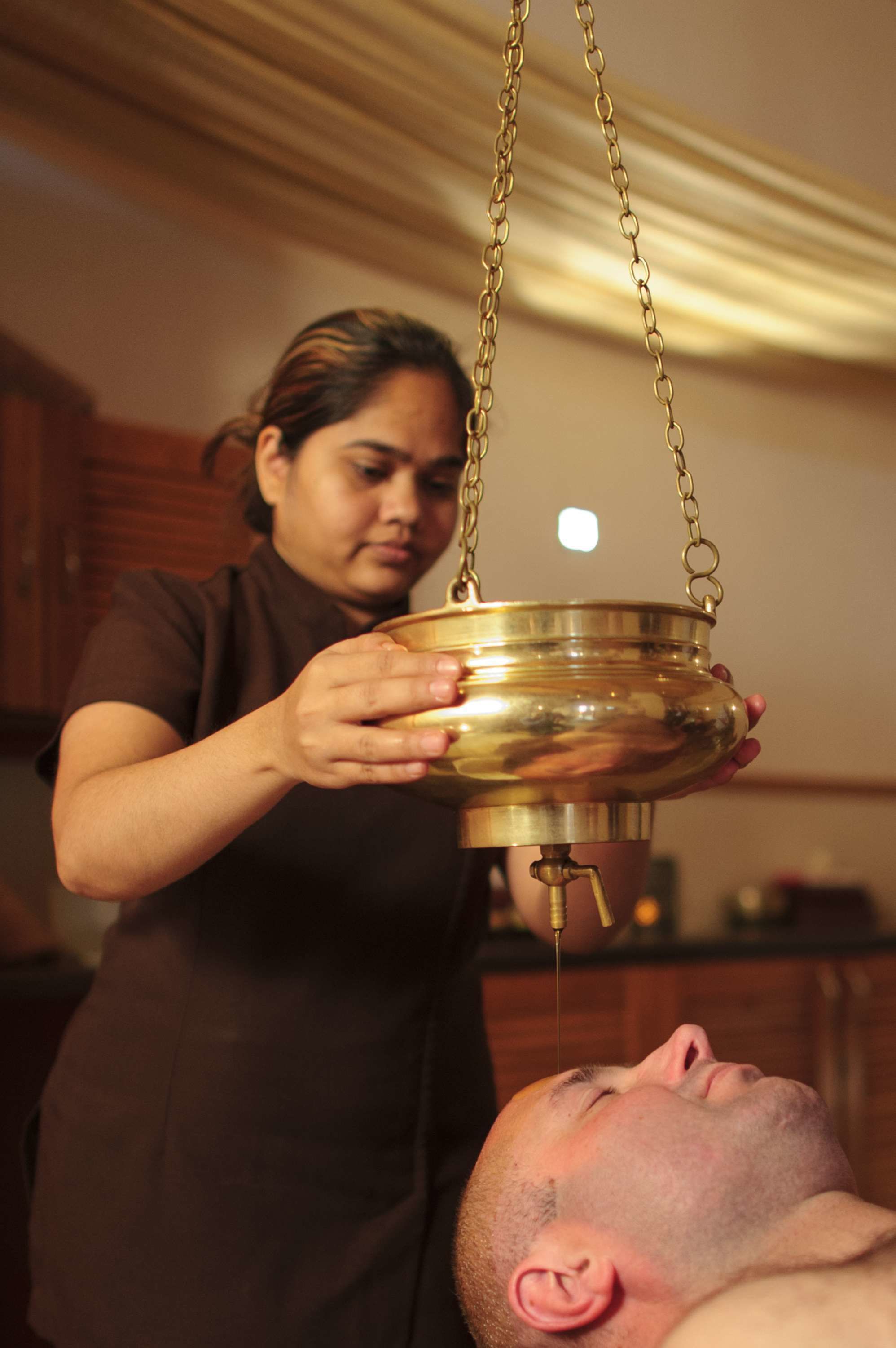 A person holding a brass container over another person's head.
