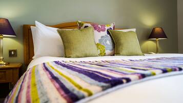 A neatly made bed with a colorful striped blanket, two green pillows, and a floral pillow on a wooden headboard. There are two bedside lamps on either side of the bed.