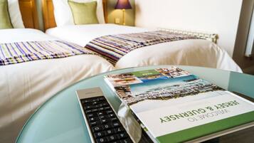 Ein Hotelzimmer mit zwei Betten, einem Schreibtisch mit Laptop und Buch sowie einer Lampe.