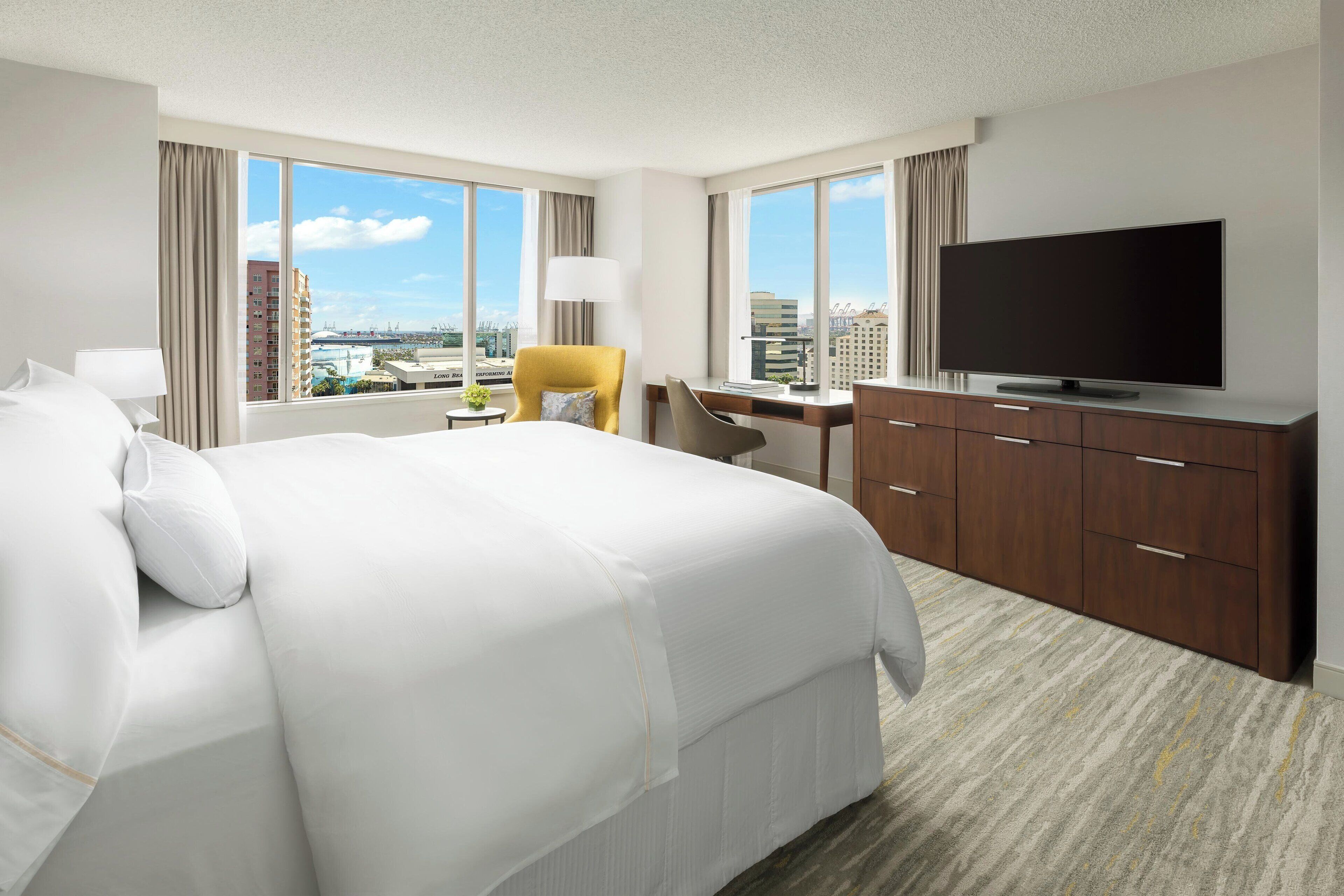 A hotel room with a large bed, a desk, a television, and a view of the cityscape.
