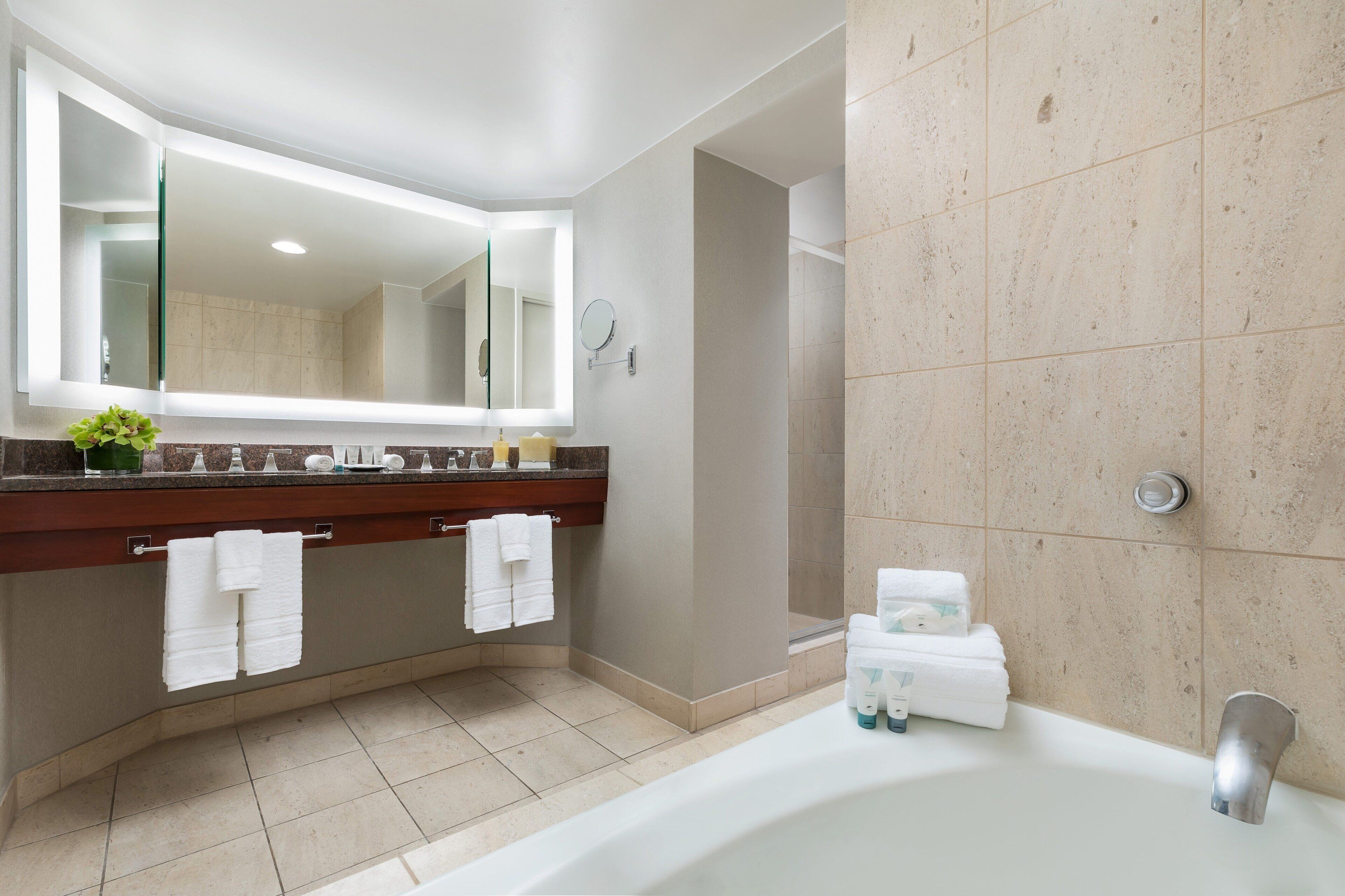 Ein modernes Badezimmer mit einem großen Spiegel, einer Badewanne und einem Waschtisch mit Arbeitsplatte.