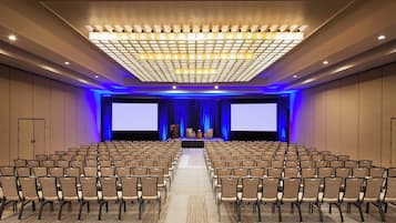 Une salle de conférence avec des rangées de chaises, un grand écran et une scène équipée d’un pupitre.