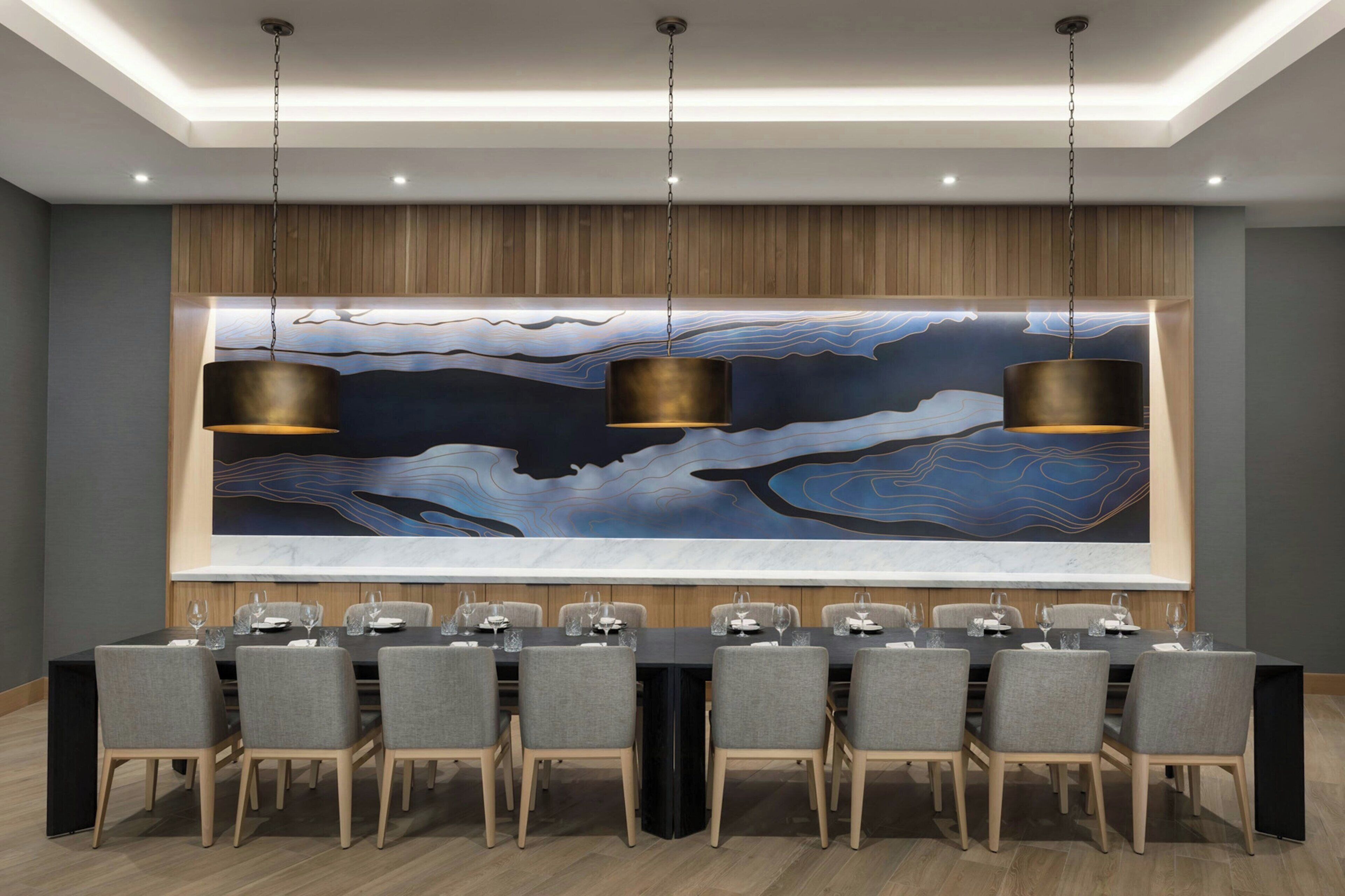 Une salle de conférence avec une longue table, des chaises grises et un grand tableau abstrait accroché au mur.