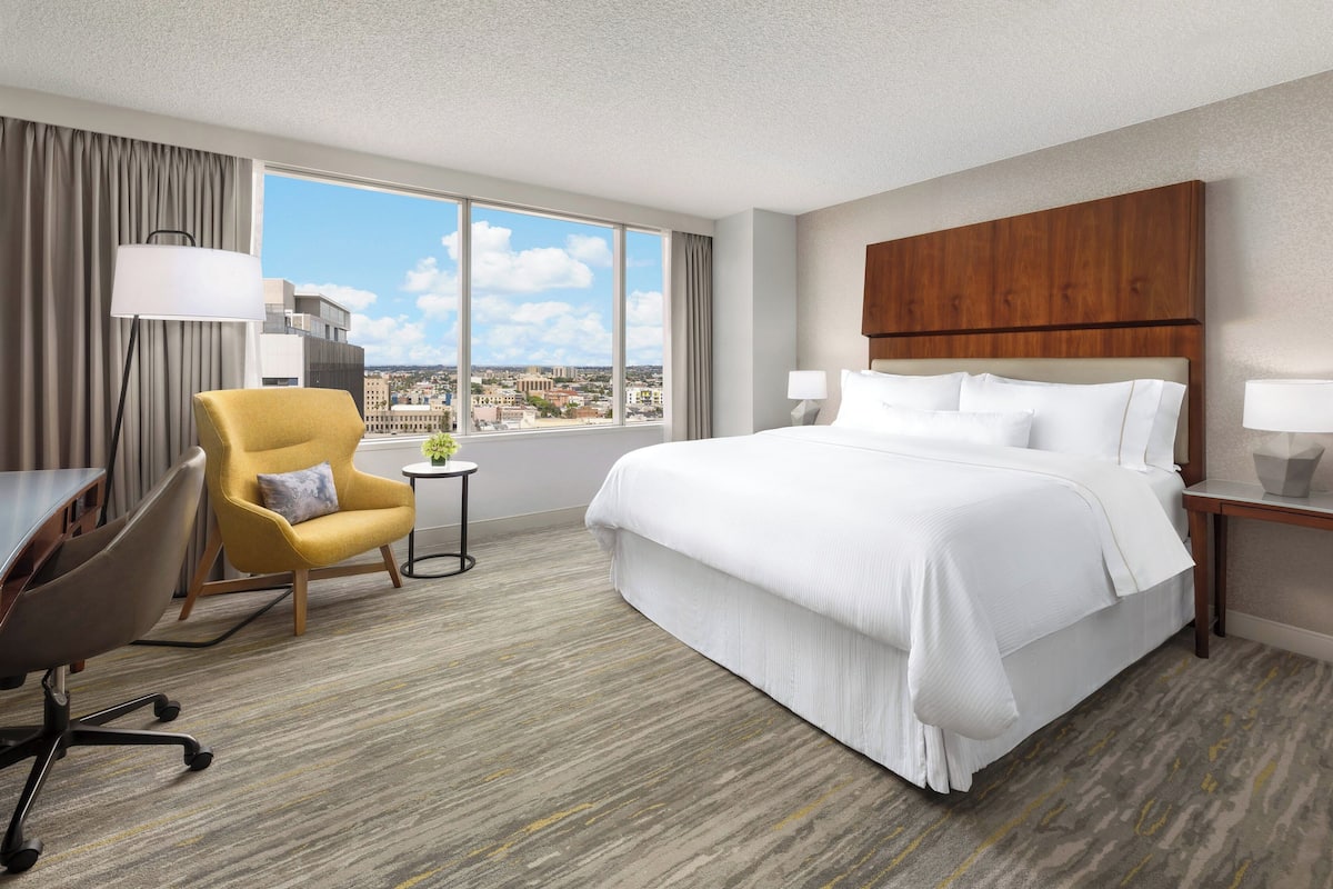 A hotel room with a large bed, a desk, a chair, and a view of the city.