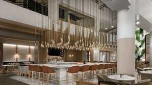 Un moderno vestíbulo de hotel con una zona de bar central, áreas de descanso y un techo alto con lámparas colgantes.