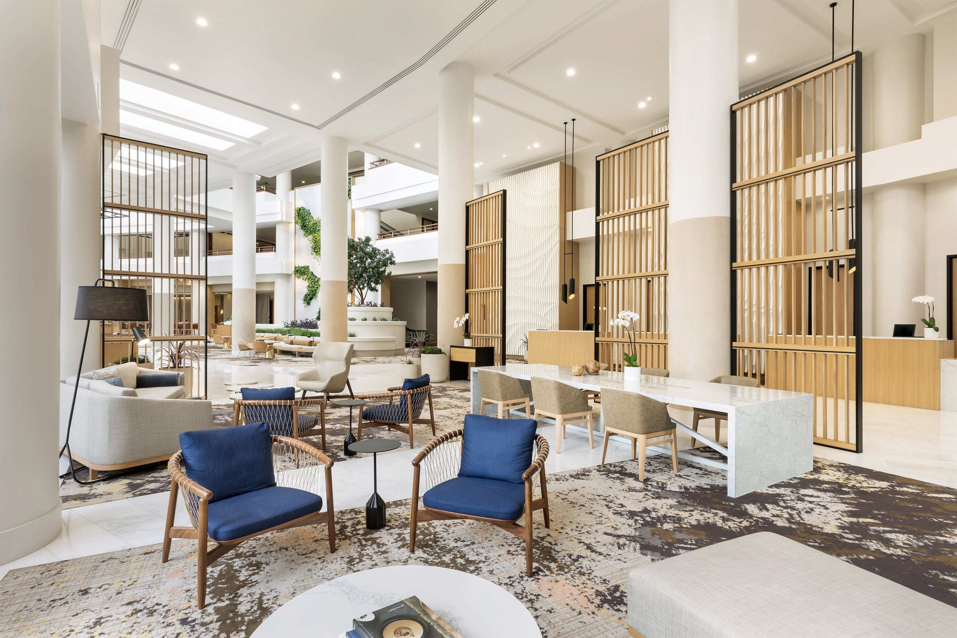 A spacious lobby with high ceilings, a central seating area with sofas and chairs, a reception desk, and large windows allowing natural light.