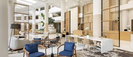 A spacious lobby with high ceilings, a central seating area with sofas and chairs, a reception desk, and large windows allowing natural light.