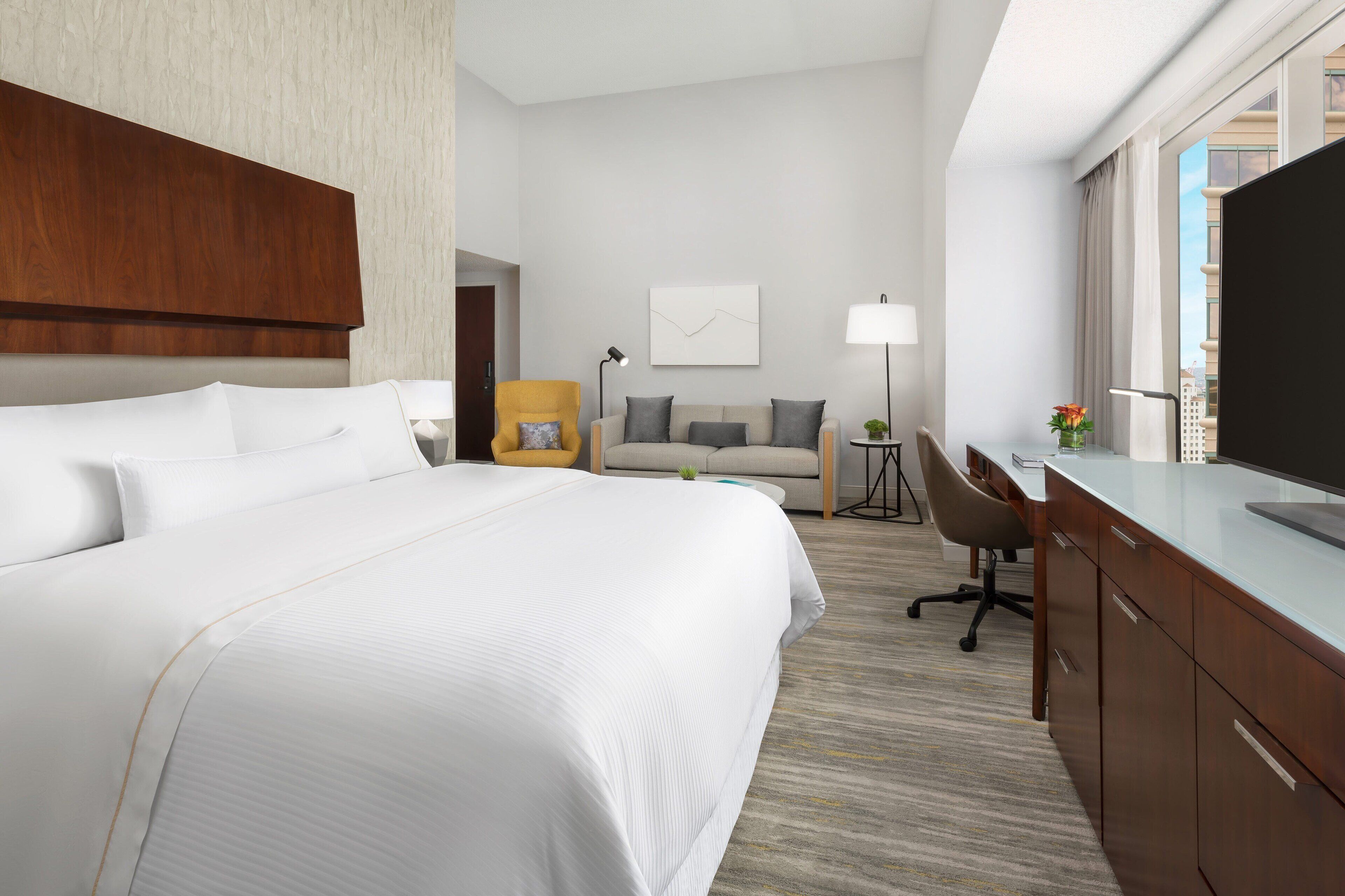 Une chambre d’hôtel avec un grand lit, un bureau, une chaise, une lampe et un téléviseur.