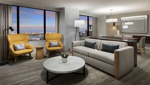 Una habitación de hotel moderna con sofá, sillones, una mesa de comedor y un ventanal con vistas a la ciudad.