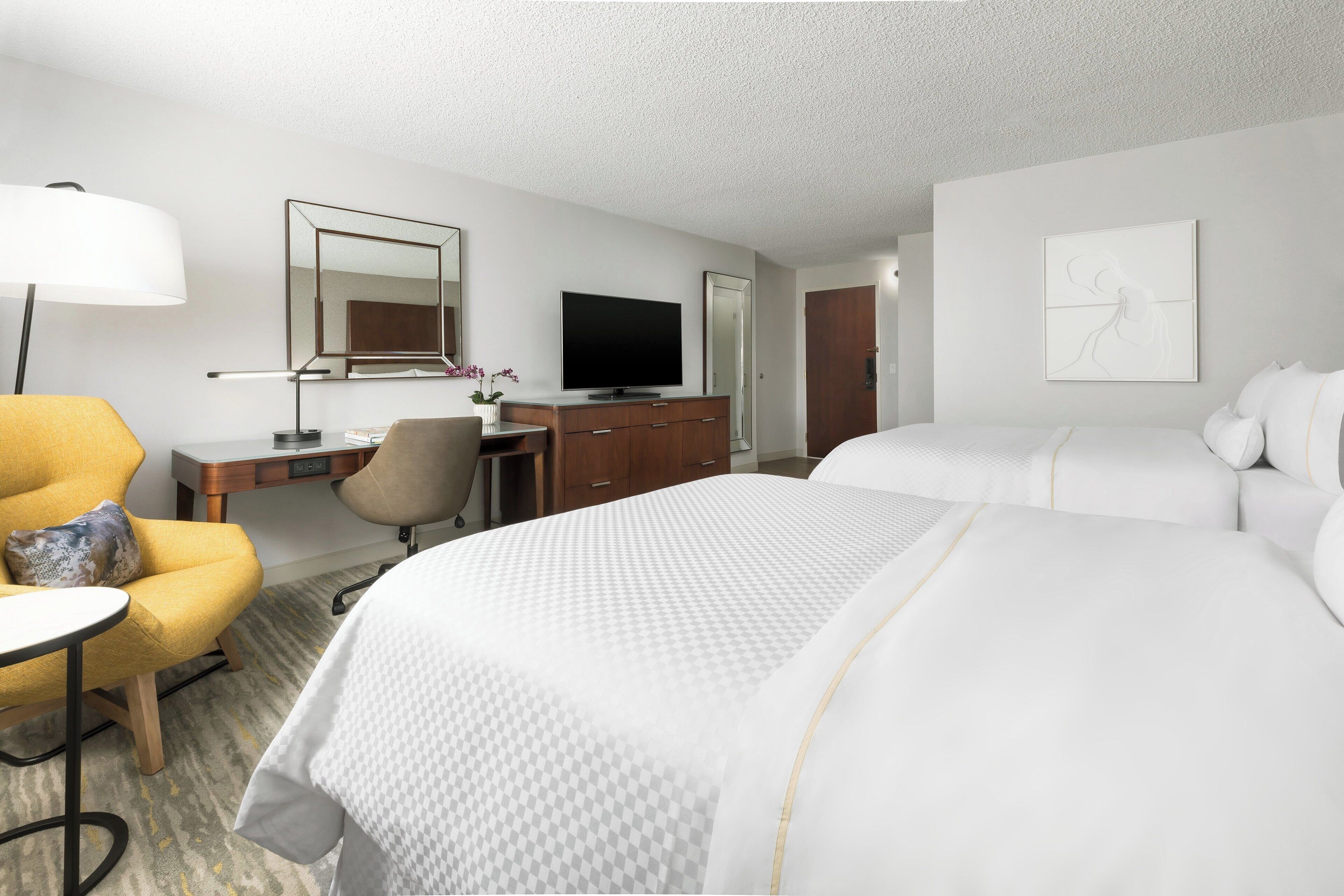Habitación de hotel con cama, escritorio con computadora, silla, lámpara y televisor.