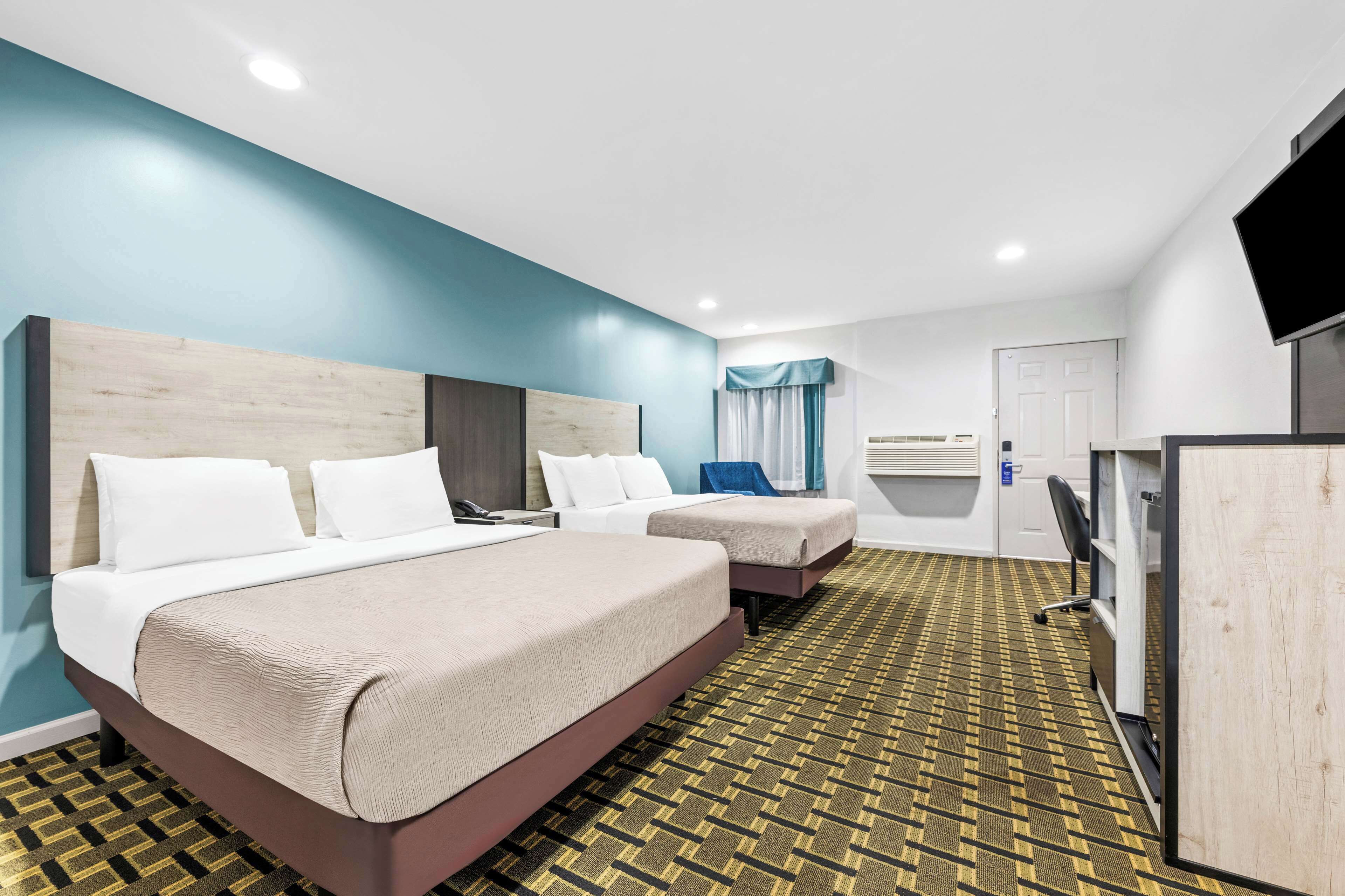 A hotel room with two beds, a TV, a desk, and a patterned carpet.