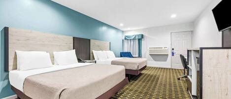 A hotel room with two beds, a TV, a desk, and a patterned carpet.