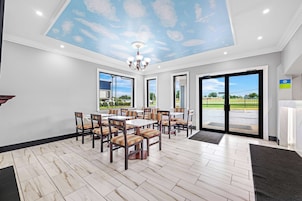 A dining area with a high ceiling, large windows, and a view of the outdoors.