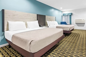 A hotel room with two beds, a wooden headboard, a patterned carpet, and a window with curtains.