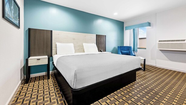 A modern hotel room with a large bed, a nightstand, a chair, and a window with blinds.