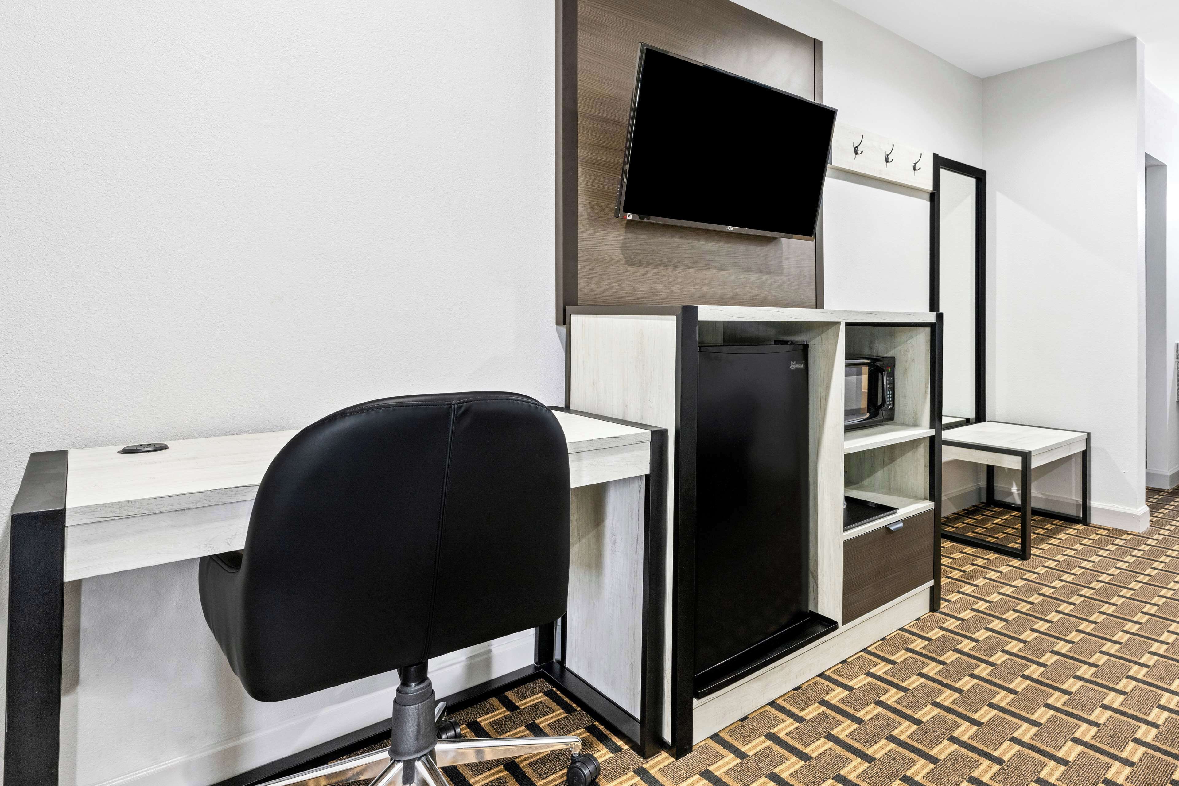 Habitación de hotel moderna con escritorio blanco, silla negra, televisor integrado y piso con diseño.