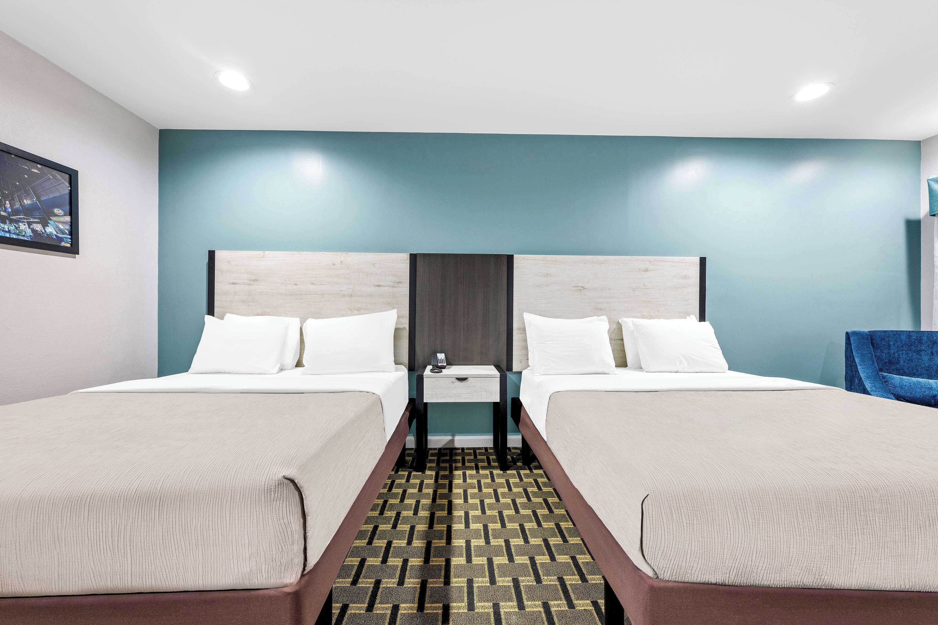 A hotel room with two beds, a nightstand, a blue wall, and a patterned carpet.