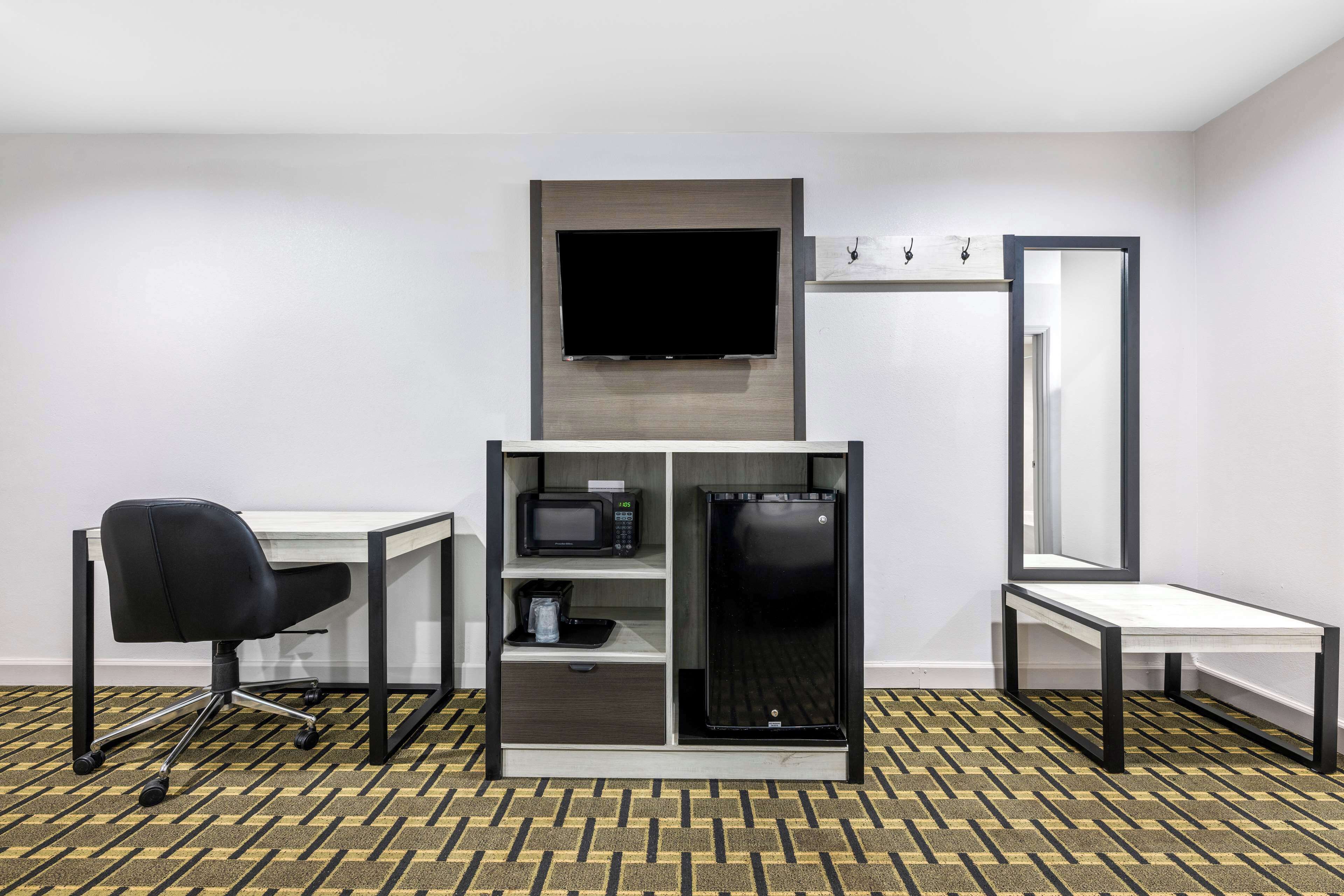 Habitación de hotel con escritorio, silla, microondas, refrigerador, televisor y espejo.