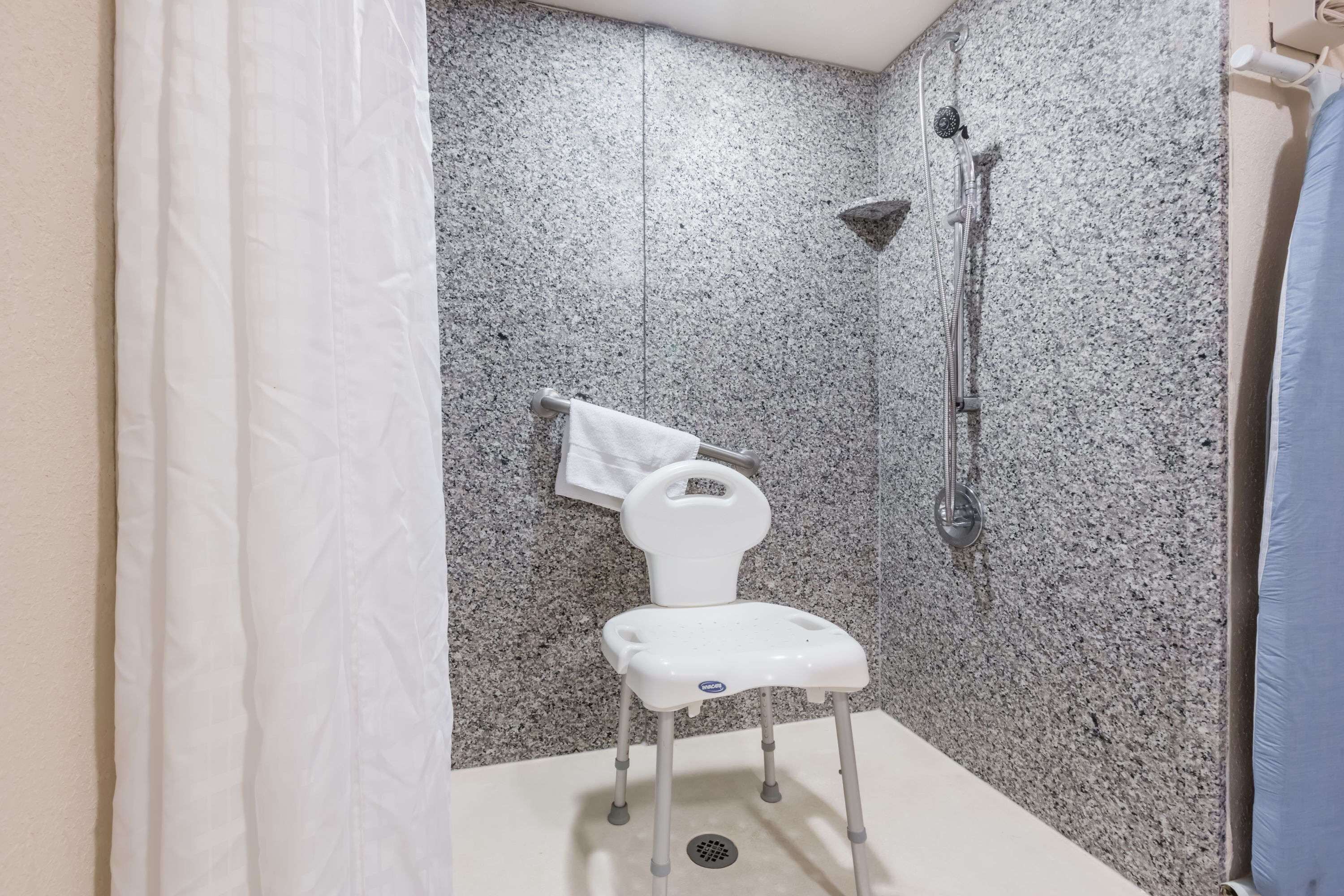 Une salle de bain avec une douche, une chaise blanche et une serviette accrochée au mur.