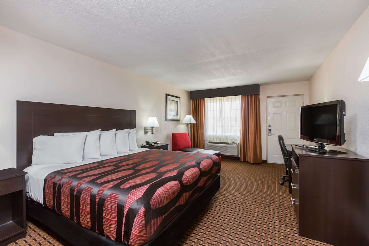 A hotel room with a large bed, a desk, a chair, a television, and a window with curtains.