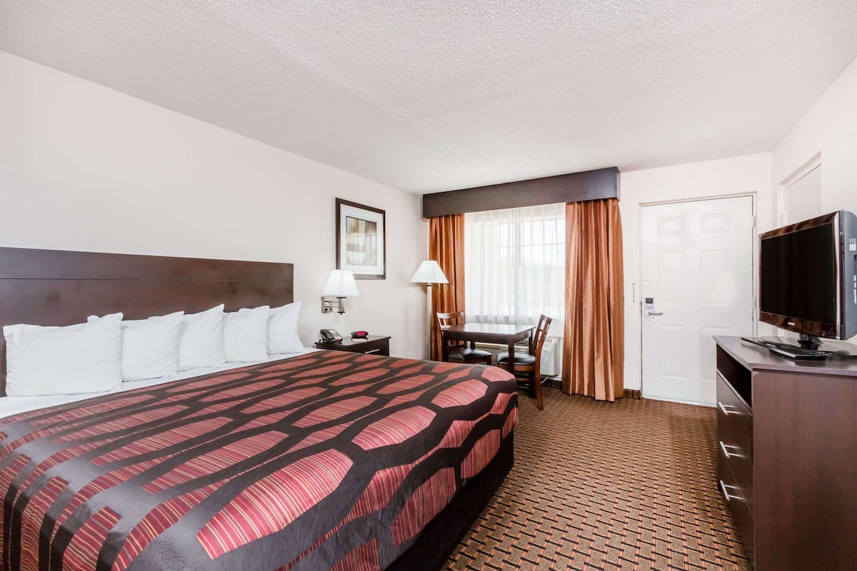A hotel room with a large bed, a desk with a chair, a television, and a door.