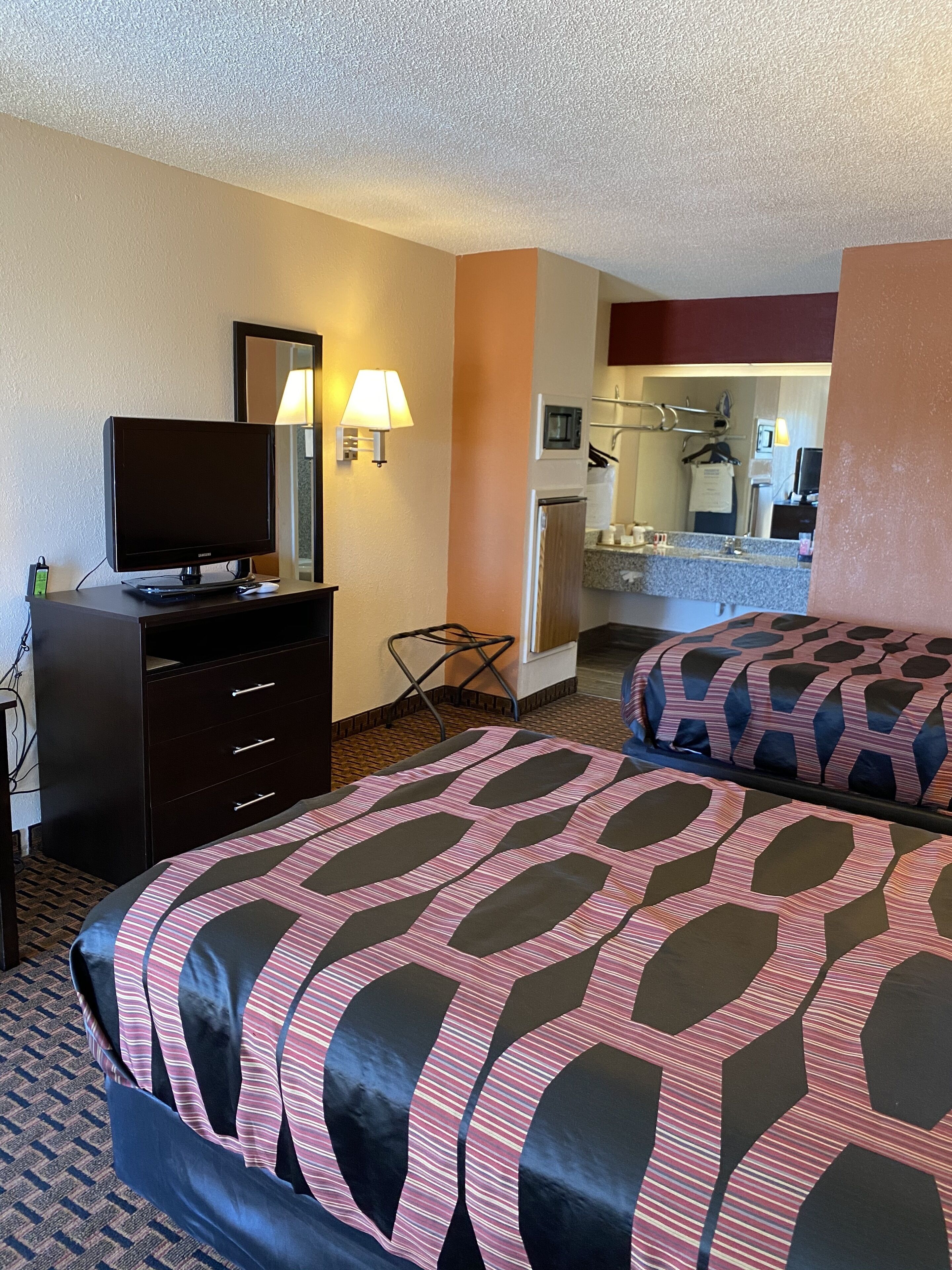 A hotel room with a bed, a dresser, a television, a lamp, and a bathroom visible through an open door.