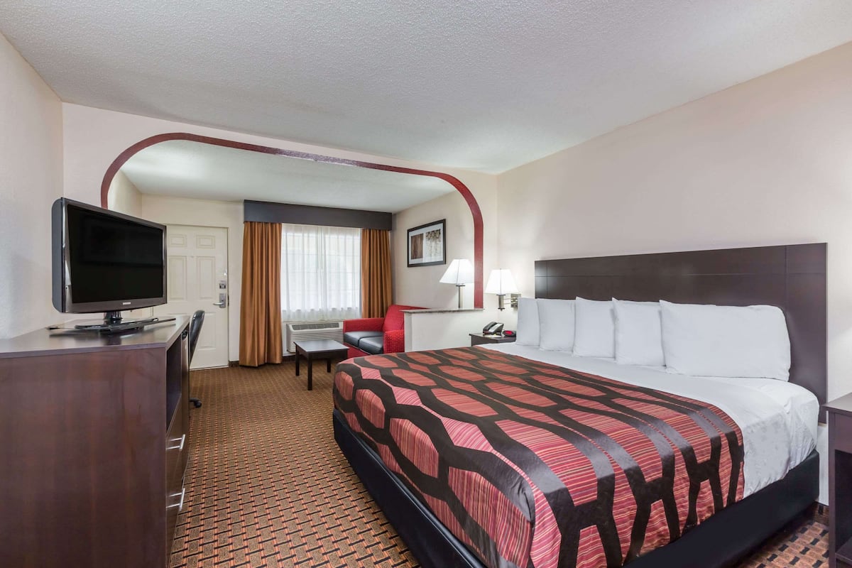 A hotel room with a large bed, a desk with a television, a chair, and a small table.