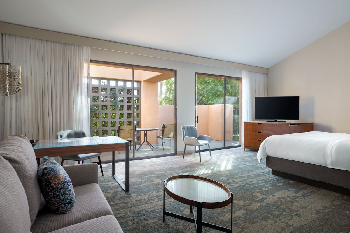 Hotelkamer met een bed, een televisie, een bank, een salontafel, een bureau en een balkon met uitzicht op groen.