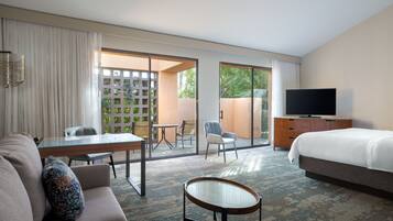 Quarto de hotel com cama, televisão, sofá, mesa de centro, escrivaninha e varanda com vista para áreas verdes.