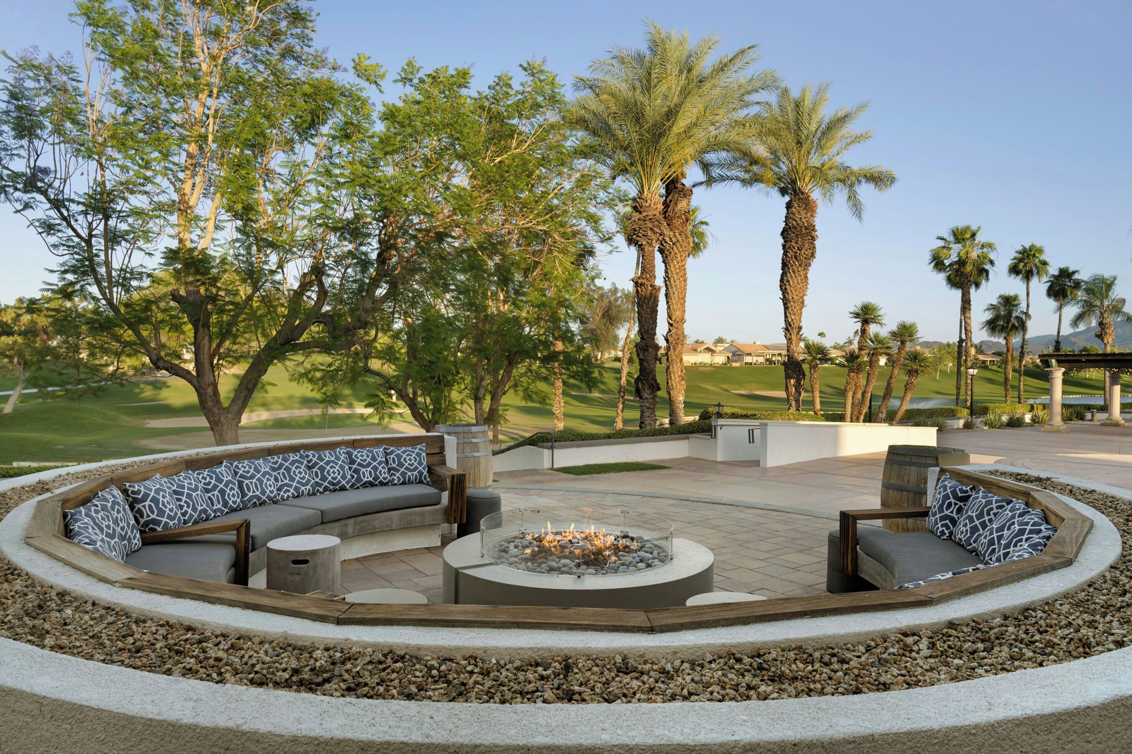 A circular outdoor seating area with a fire pit, surrounded by a low stone wall, and overlooking a golf course.