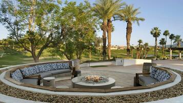 A circular outdoor seating area with a fire pit, surrounded by a low stone wall, and overlooking a golf course.