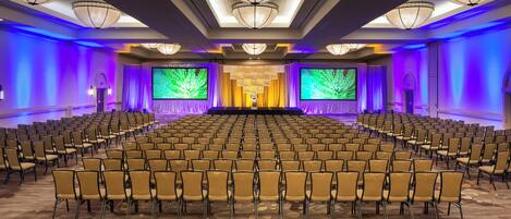 A conference room with rows of chairs, large screens, and a stage.