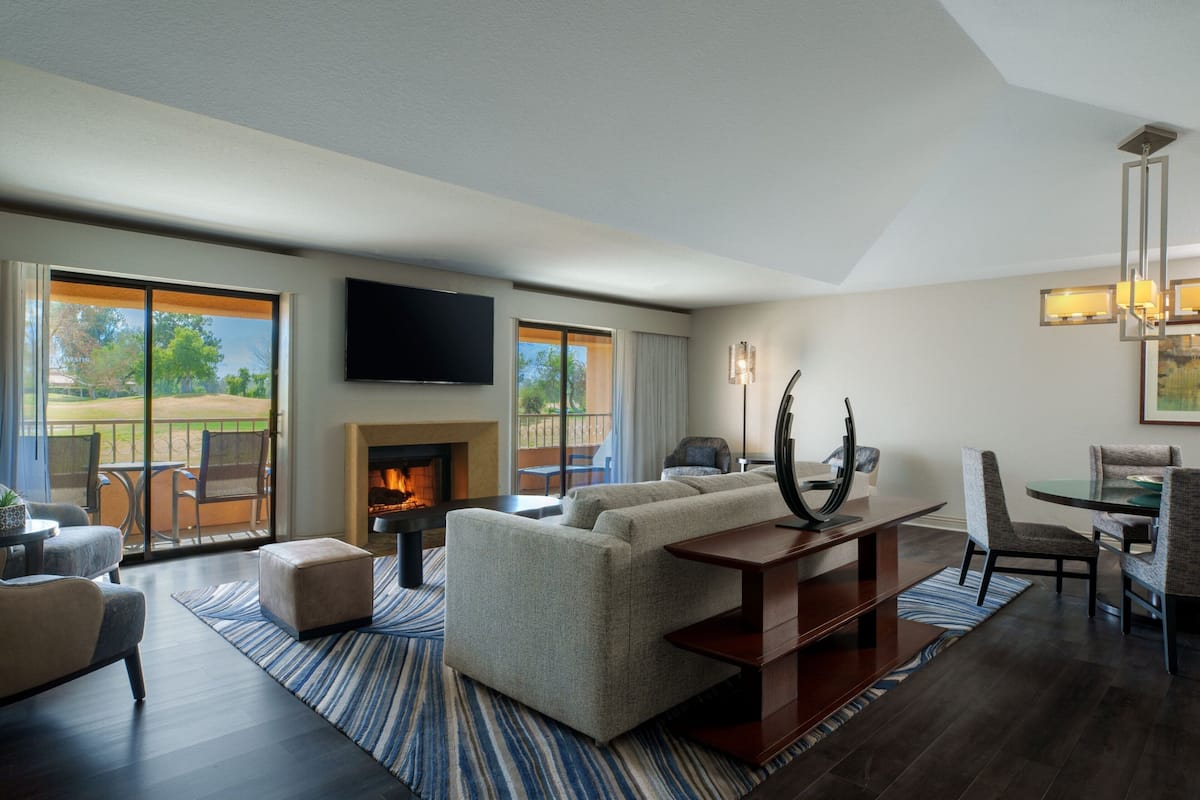 Een ruime woonkamer met een open haard, een flatscreen-tv aan de wand en een eethoek met een tafel en stoelen.
