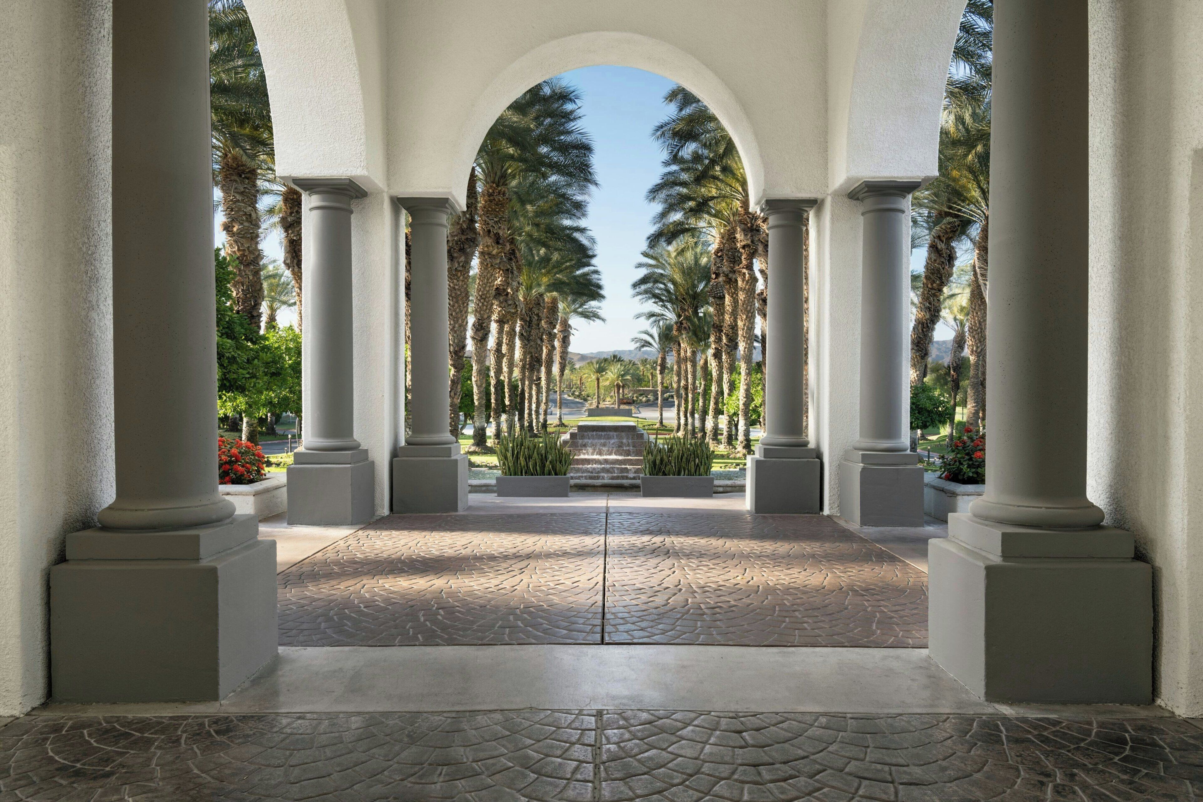 Une allée couverte, bordée de colonnes et de palmiers.
