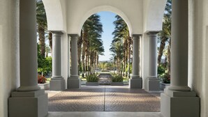 A covered walkway with columns and palm trees.
