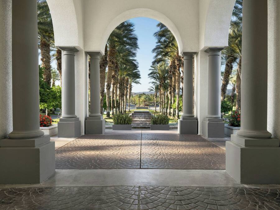 Une allée couverte, bordée de colonnes et de palmiers.