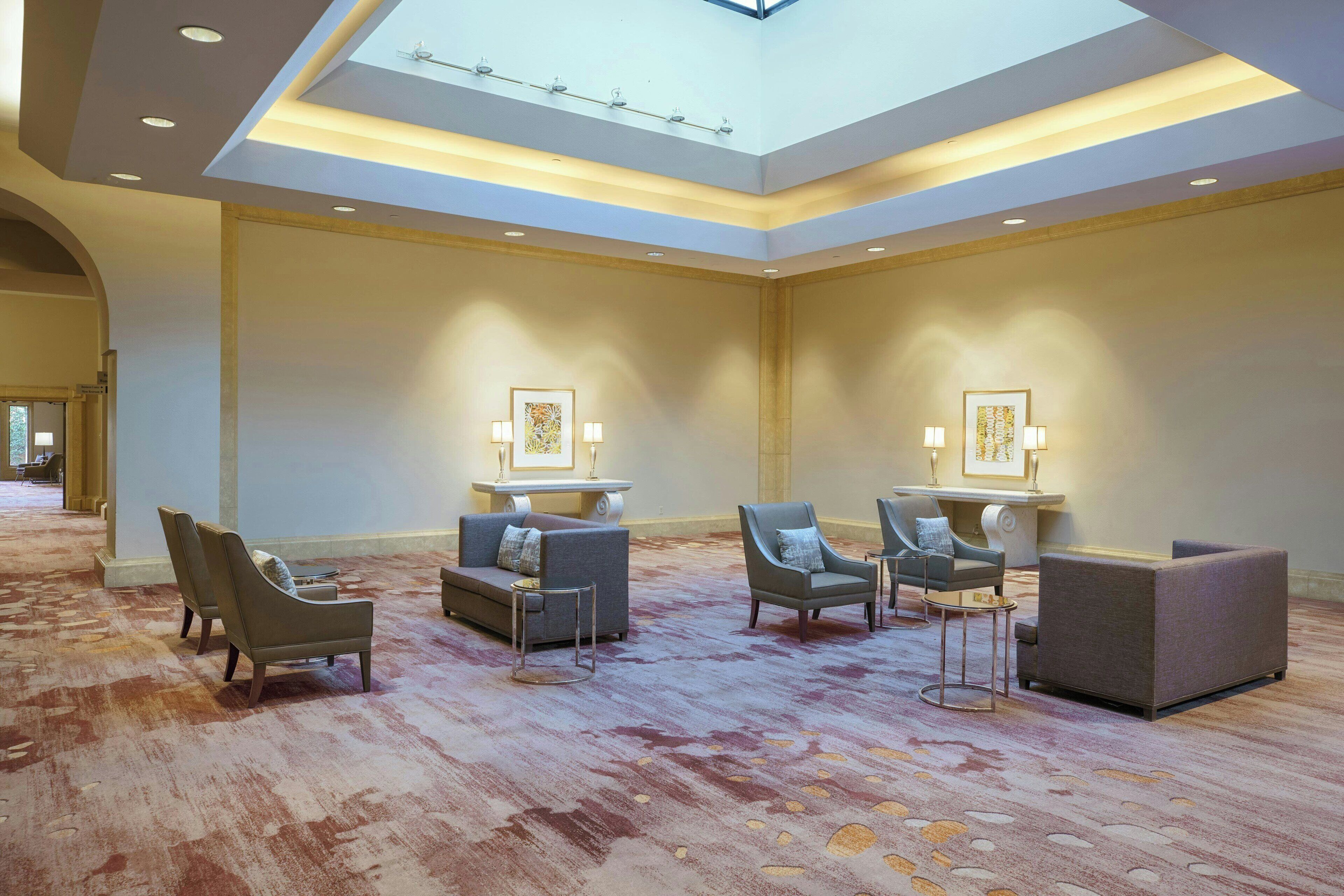 Un hall d’entrée spacieux avec un plafond haut, des luminaires encastrés et une verrière. On y trouve plusieurs coins salon avec des canapés et des fauteuils.