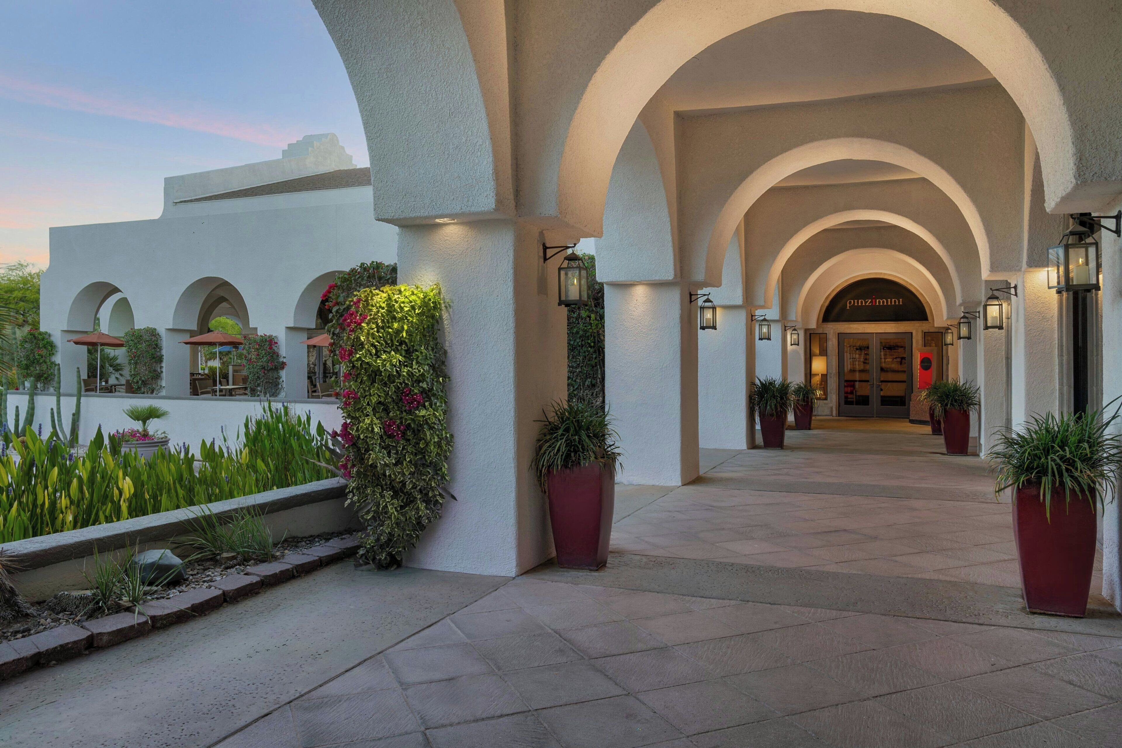 Ingresso di un hotel con portici ad arco, piante in vaso e un cartello con la scritta 'pinzimini'.