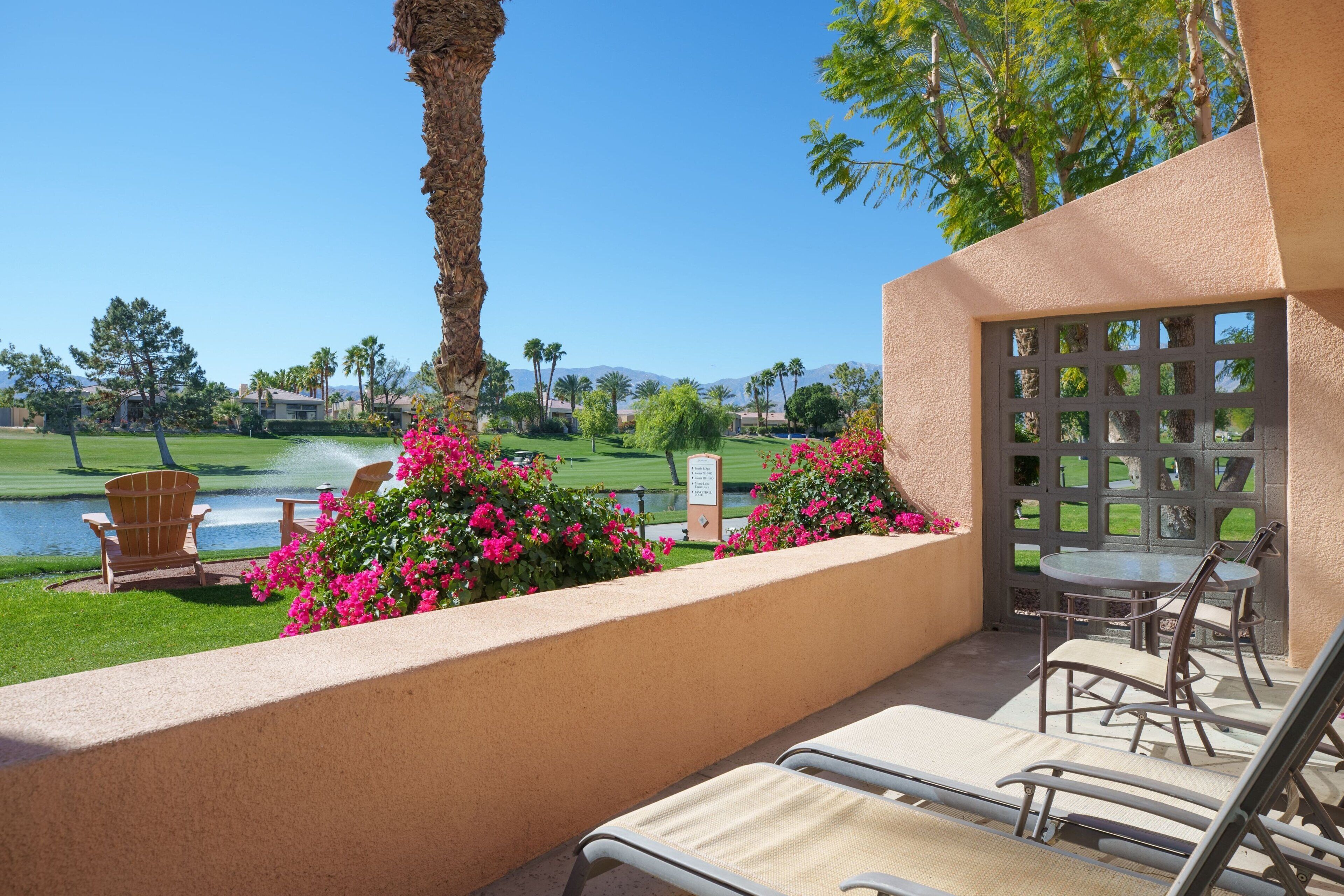 Un patio con sillones de descanso, una mesa y vistas a un campo de golf y un cuerpo de agua.