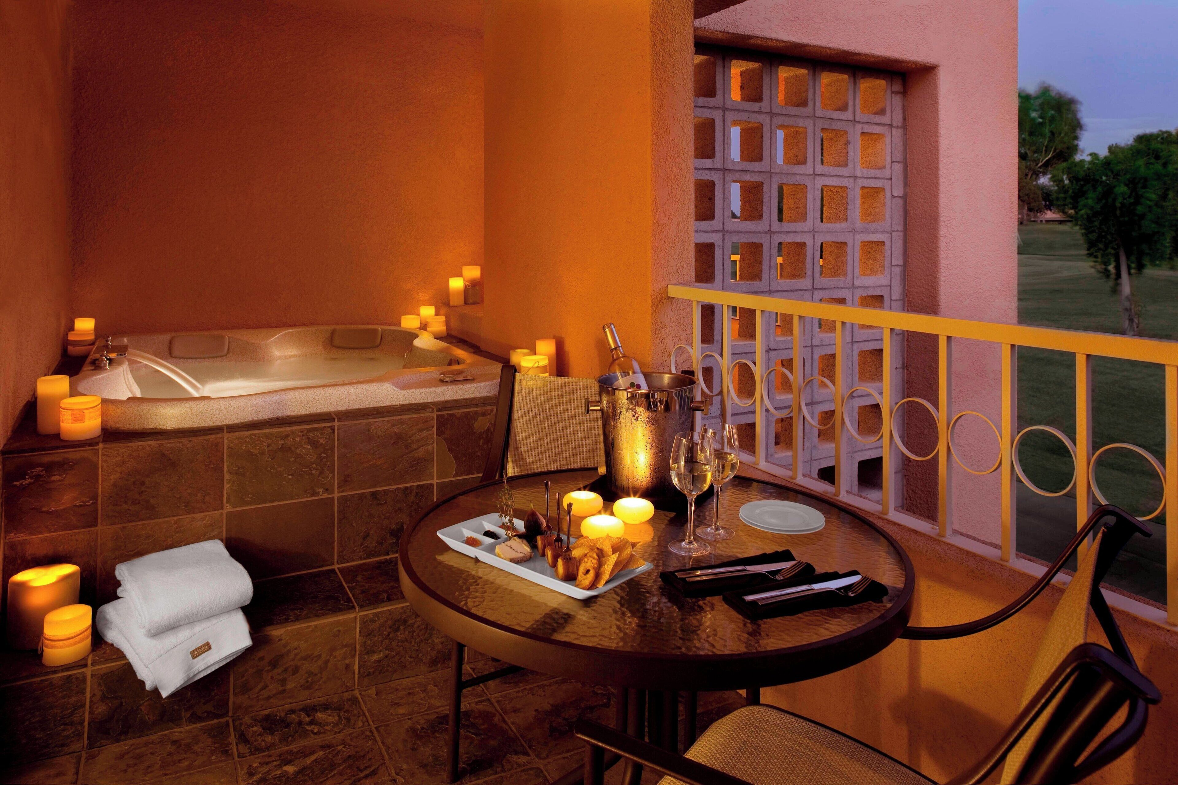 A balcony with a hot tub, candles, and a table set for a meal.