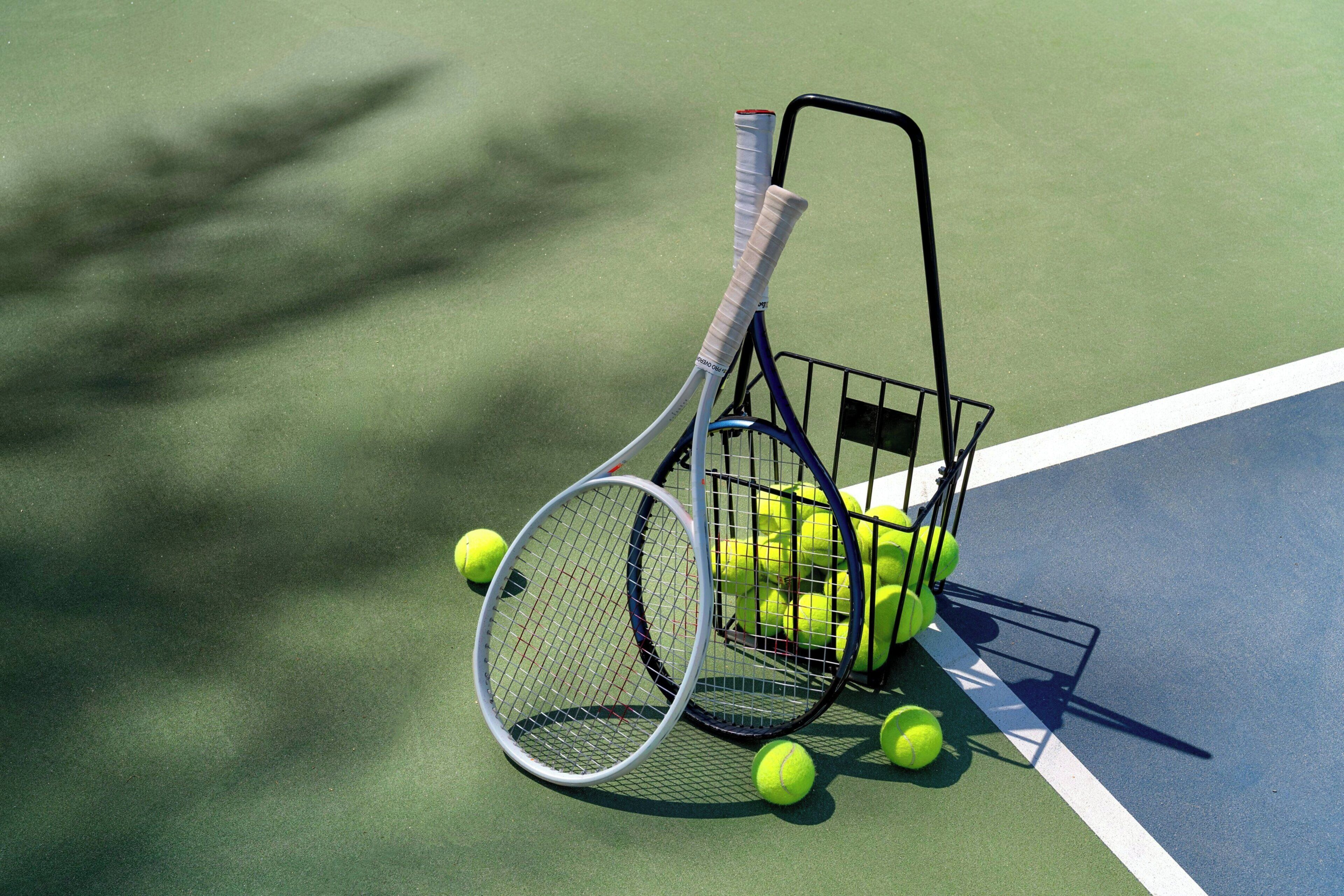 A tennis court with a rack of tennis balls and rackets.