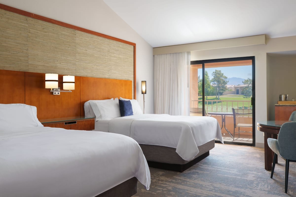 Een hotelkamer met twee bedden, een bureau en uitzicht op een golfbaan.