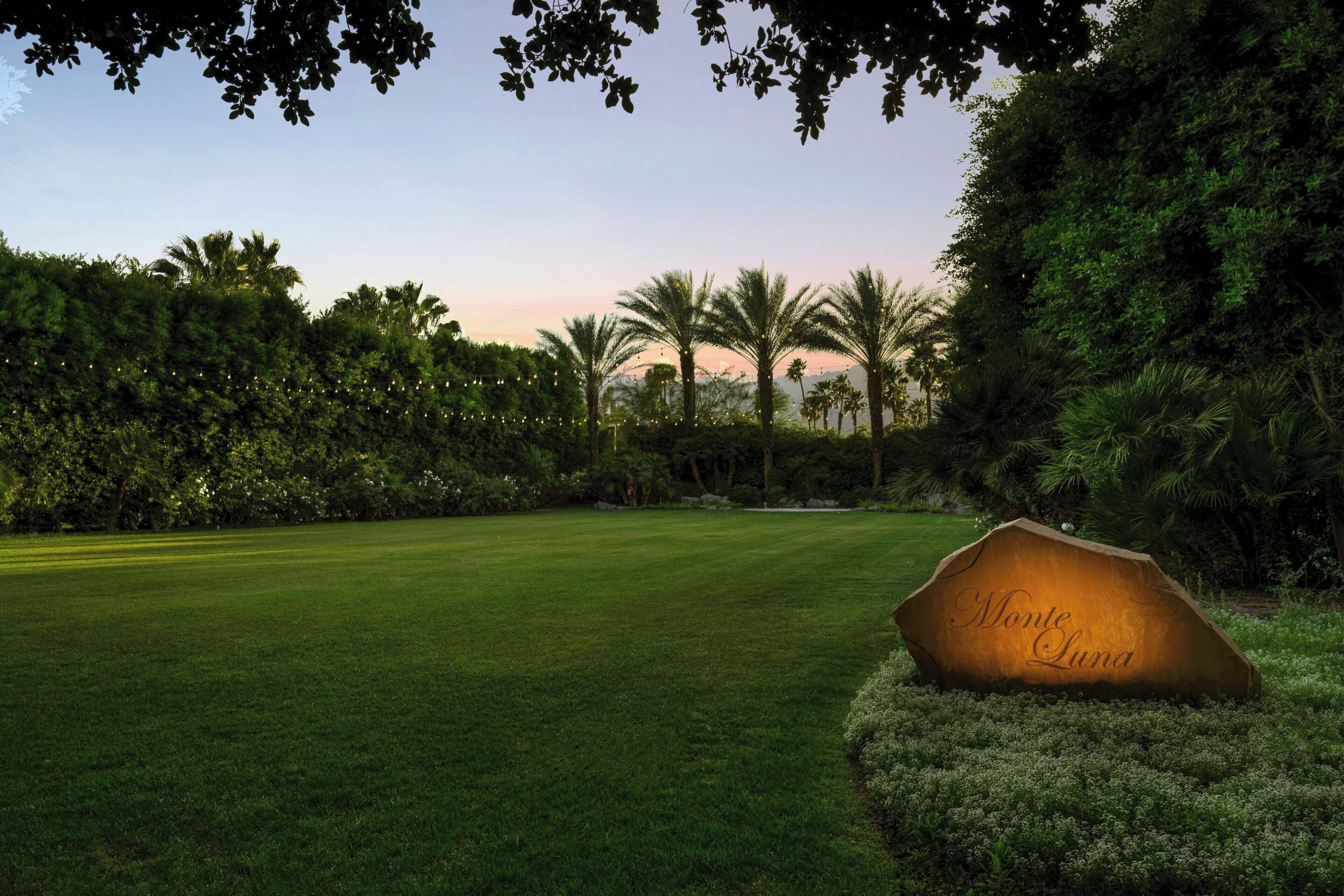 A golf course with a sign reading 'Monte Luna' surrounded by lush greenery and palm trees.