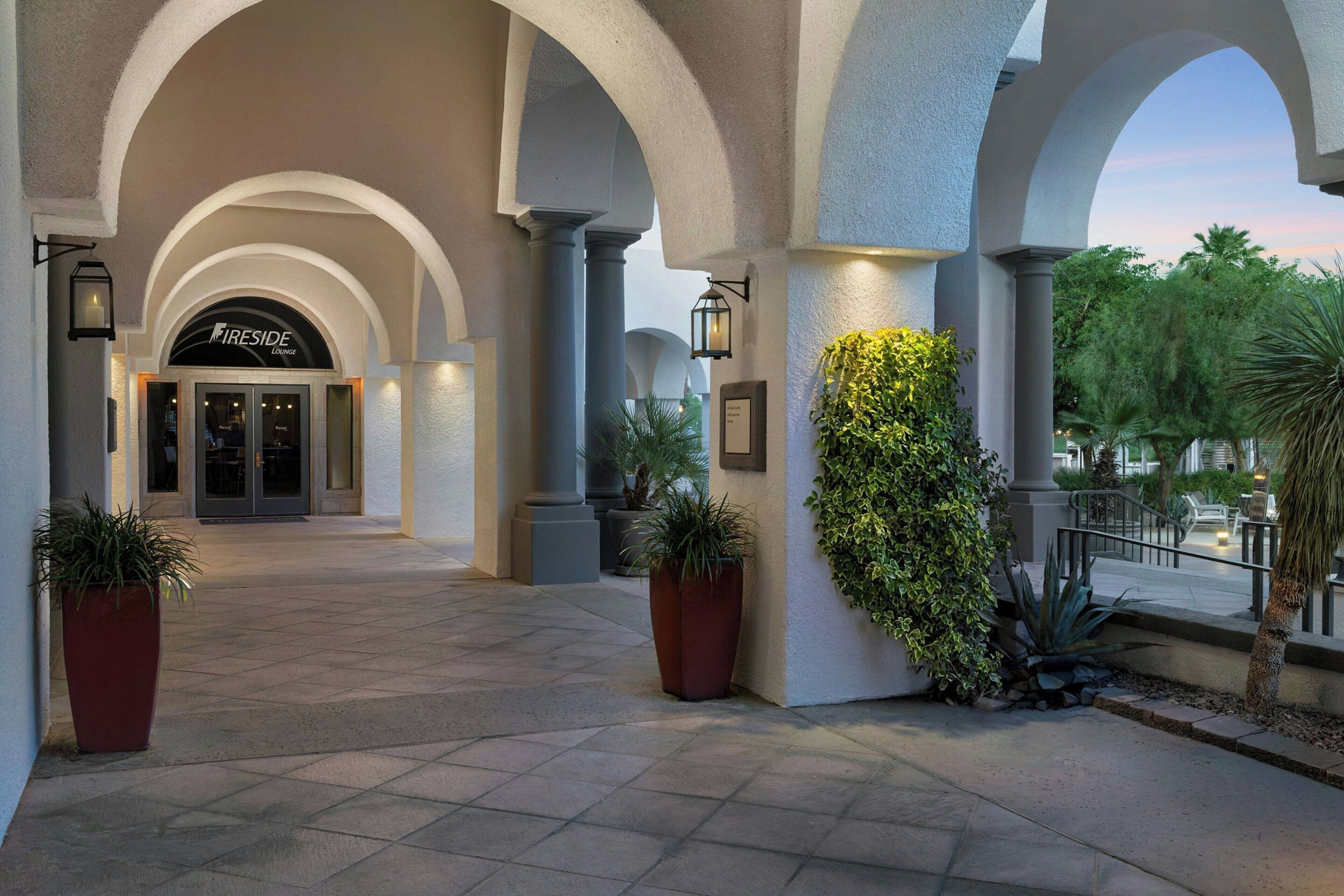 Entrada de hotel con columnas abovedadas, un letrero que dice 'Fireside Lounge' y plantas en macetas.
