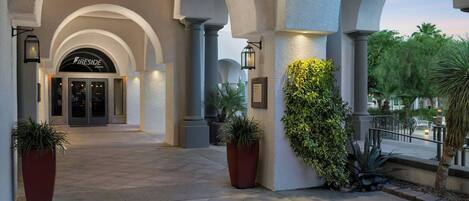 Entrada de hotel con columnas abovedadas, un letrero que dice 'Fireside Lounge' y plantas en macetas.