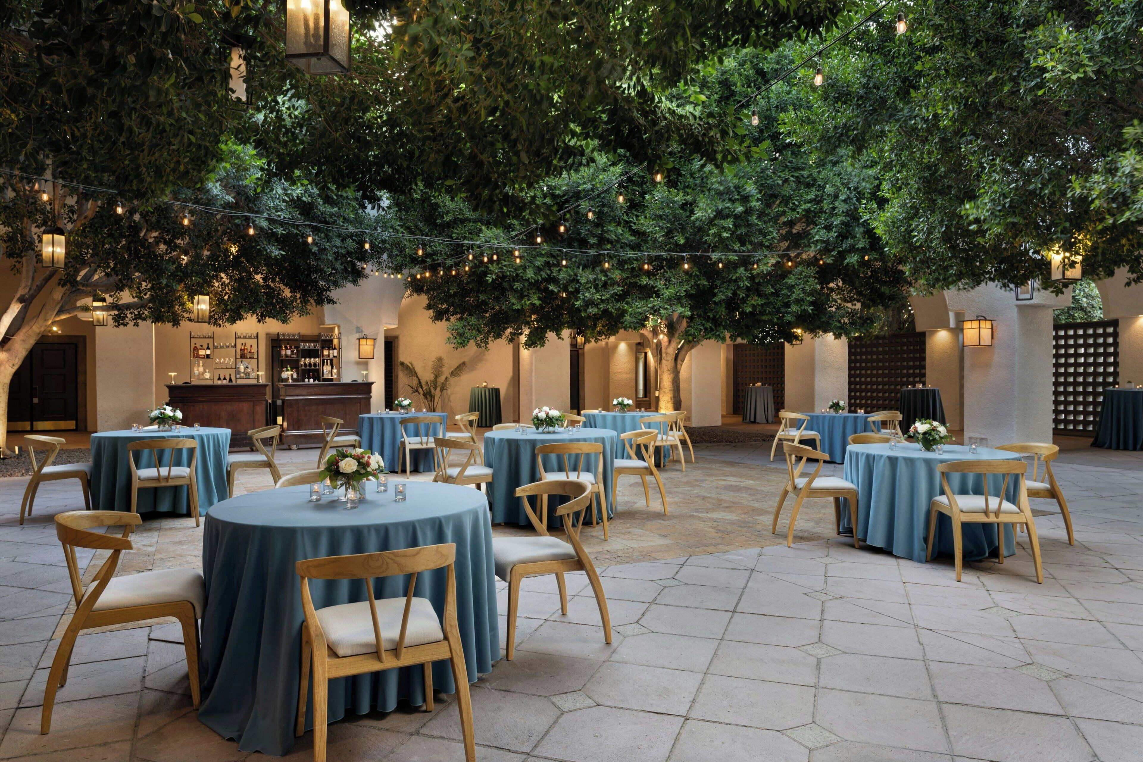 Une terrasse extérieure avec des tables et des chaises rondes, des guirlandes lumineuses et un décor composé d’arbres.