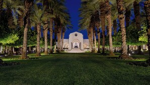 A building with a central entrance, flanked by palm trees, and a well-maintained lawn in front.