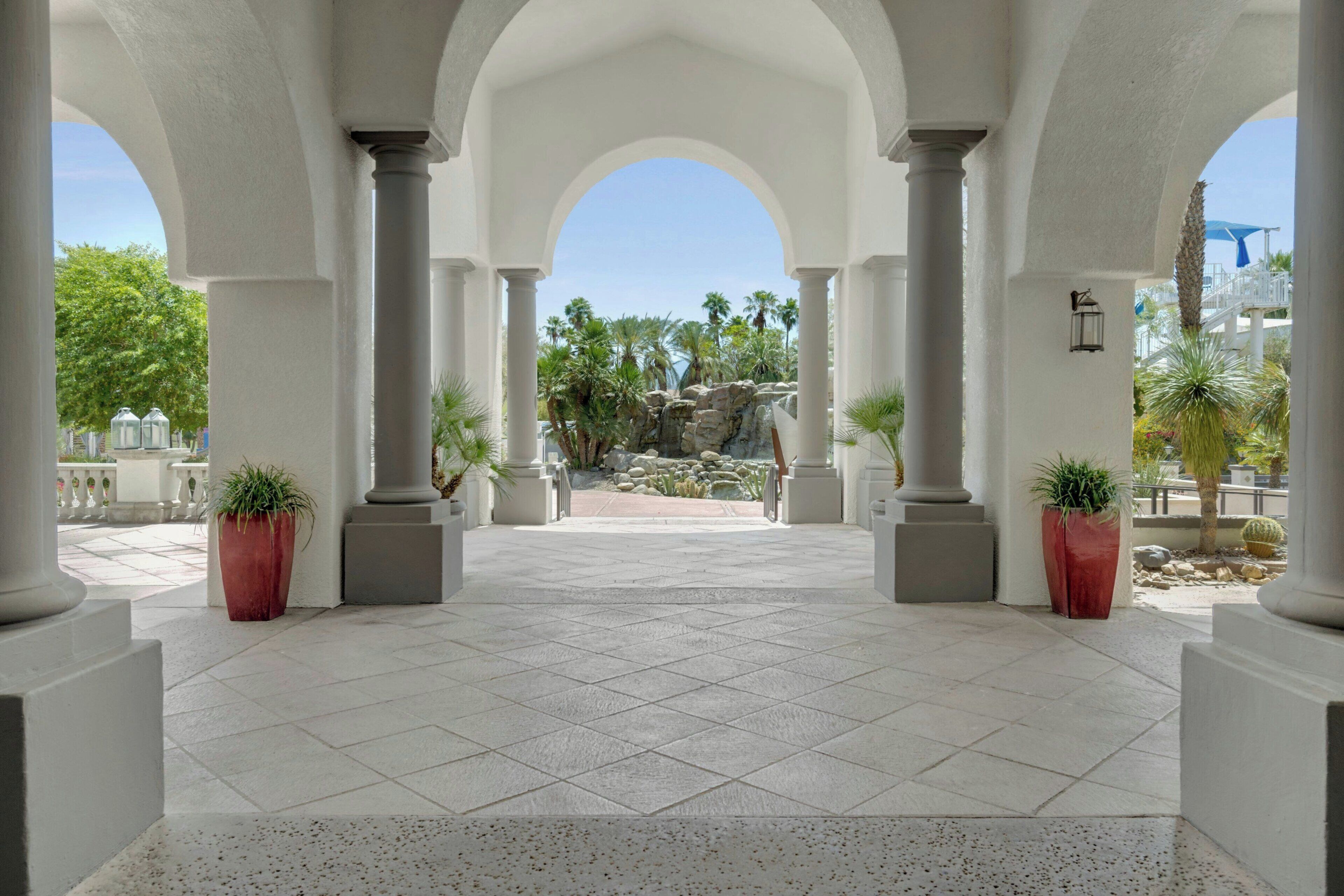 Un patio amplio con columnas blancas, plantas en macetas y vistas a un paisaje rocoso.